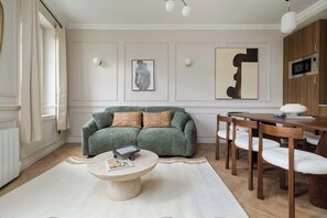 Ein Wohnzimmer mit einem grünen Sofa, einem runden Couchtisch und einem Essbereich mit Holzsesseln und einem Tisch.