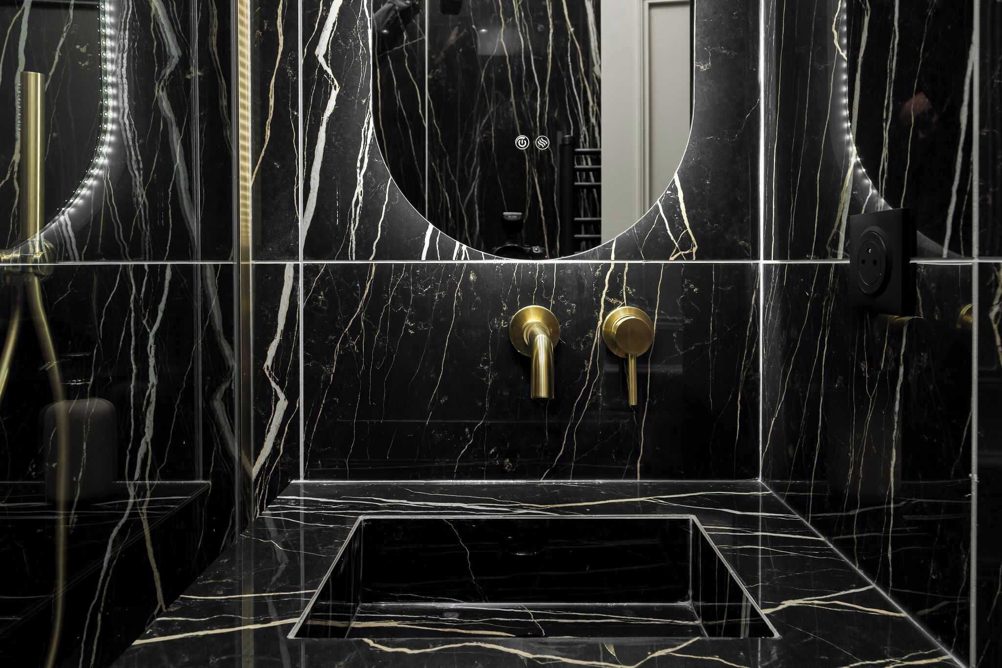 A bathroom with black marble walls, gold fixtures, and a mirror.