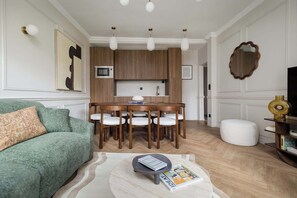 Ein modernes Wohnzimmer mit einem grünen Sofa, einem runden Couchtisch, einem Essbereich mit Holzkästen und einer Küche mit Mikrowelle.