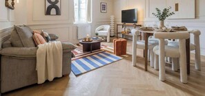 Un salon comprenant un canapé, une table basse, un téléviseur, une table à manger avec des chaises et un tapis à rayures.