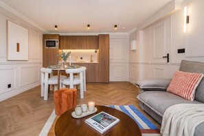 Un salon moderne comprenant un coin repas, une cuisine avec des meubles en bois et un canapé gris agrémenté d’un coussin rouge.
