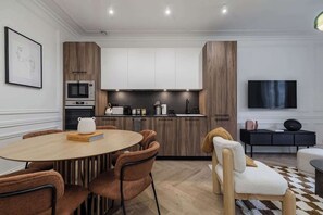 A modern kitchen with built-in appliances, a dining area with a round table and chairs, and a flat-screen TV mounted on the wall. - Terrific apartment 2BDR/6PAX next the Eiffel Tower (Paris)