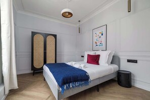 A modern bedroom with a bed, a blue throw blanket, a red pillow, a framed picture, a black trash bin, and a white ceiling light. - Terrific apartment 2BDR/6PAX next the Eiffel Tower (Paris)