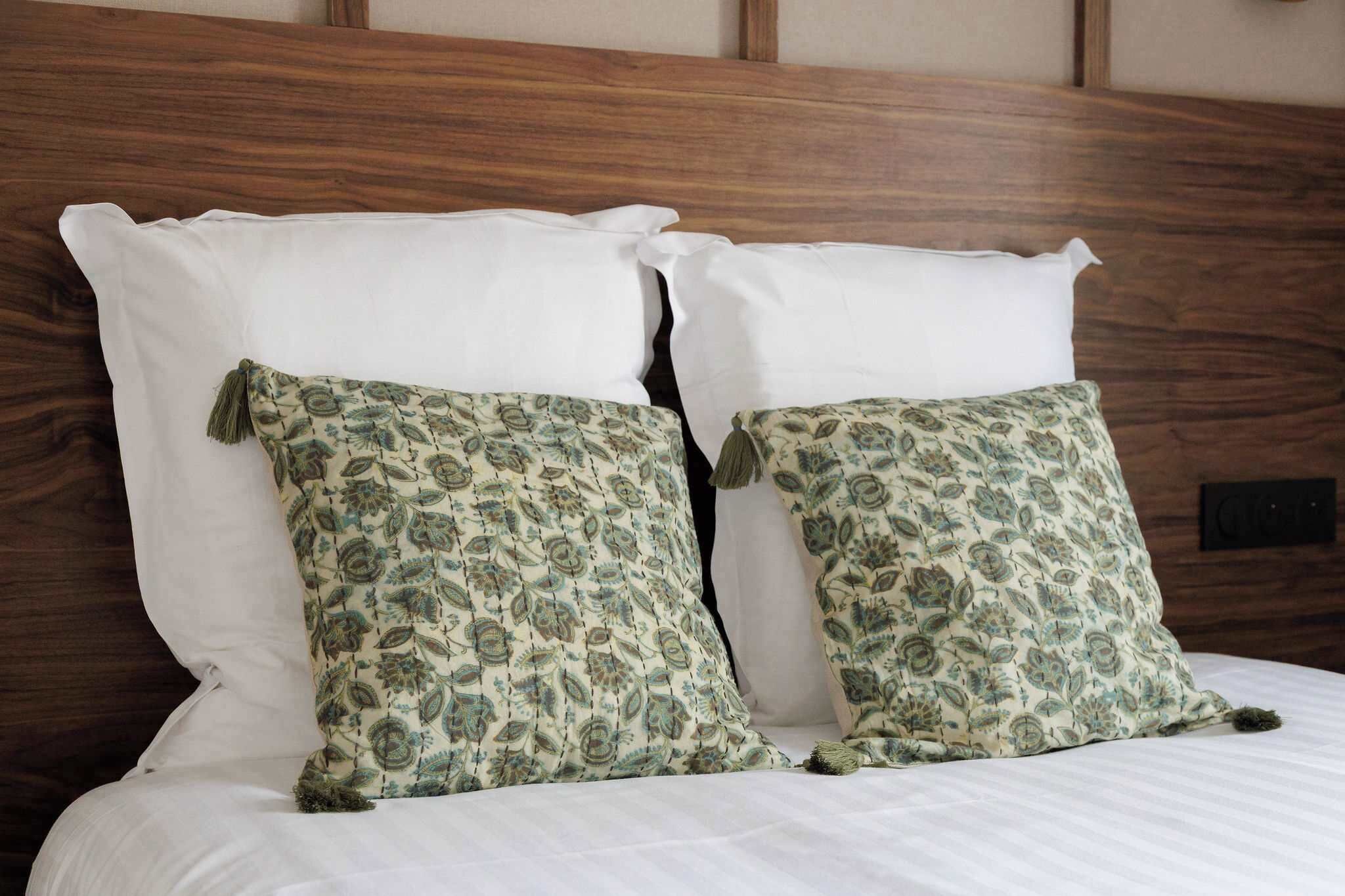 Un lit avec des oreillers blancs et deux coussins décoratifs à motifs cachemire.