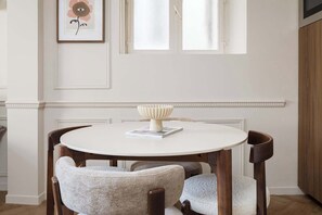 Uma mesa de jantar redonda com toalha branca, rodeada por quatro cadeiras estofadas com tecido claro.