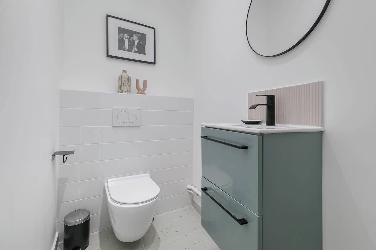 A modern bathroom with a toilet, a cabinet with drawers, a framed photo on the wall, and a towel rack.
