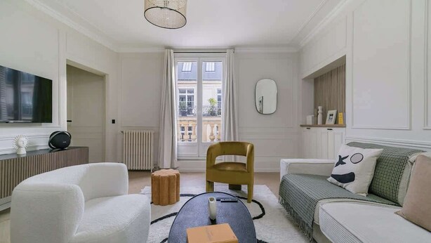 Un salon moderne avec un canapé, un fauteuil et une table basse sur laquelle repose une boîte Louis Vuitton.