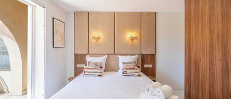 Quarto de hotel com uma cama grande, duas mesas de cabeceira, um painel de cabeceira de madeira e vista para o exterior.