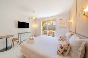 Una habitación de hotel con cama, televisión, zona de comedor y balcón.