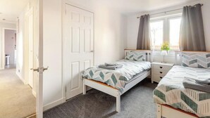 Een slaapkamer met een bed, een nachtkastje, een raam met gordijnen en een deur.