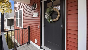 Uma casa com porta preta, placa com o número '51-1', um candeeiro preto e uma grinalda.