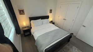 A bedroom with a bed, bedside tables with lamps, a wardrobe, and a window with blinds. - Cozy and new self contained apartment in our home in Mission, British Columbia (Mission)