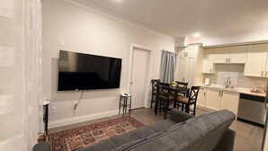 A living room with a grey sofa, a flat-screen TV, a dining table with chairs, and a kitchen area with white cabinets and a dishwasher. - Cozy and new self contained apartment in our home in Mission, British Columbia (Mission)