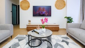 Ein modernes Wohnzimmer mit Flachbildfernseher, rundem Couchtisch, zwei Sofas, einem Holzschrank und einer Topfpflanze.