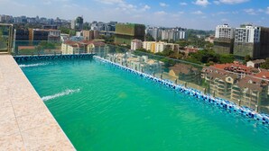 Ein Pool auf dem Dach mit Blick auf die Stadtlandschaft, bewölkter Himmel und Fliesenveranda.