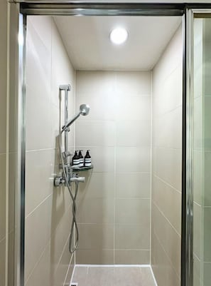En dusch med en glasdörr, ett duschmunstycke som kan hållas i handen och en hylla med flaskor.
