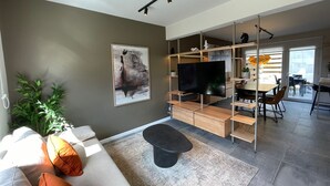 A modern living room with a sofa, a black ottoman, a flat-screen TV, and a painting on the wall.