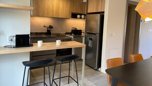 A modern kitchen with wooden cabinets, a stainless steel refrigerator, a gas stove, and a bar area with stools.