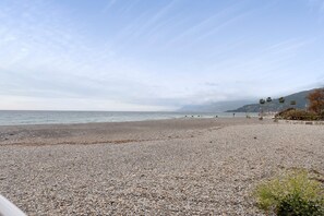 A pebbled beach with a fence and palm trees in the background. - Holiday Home 'Perla Azzurra di Riviera' with Sea View, Balcony and Air Conditioning (Ventimiglia)