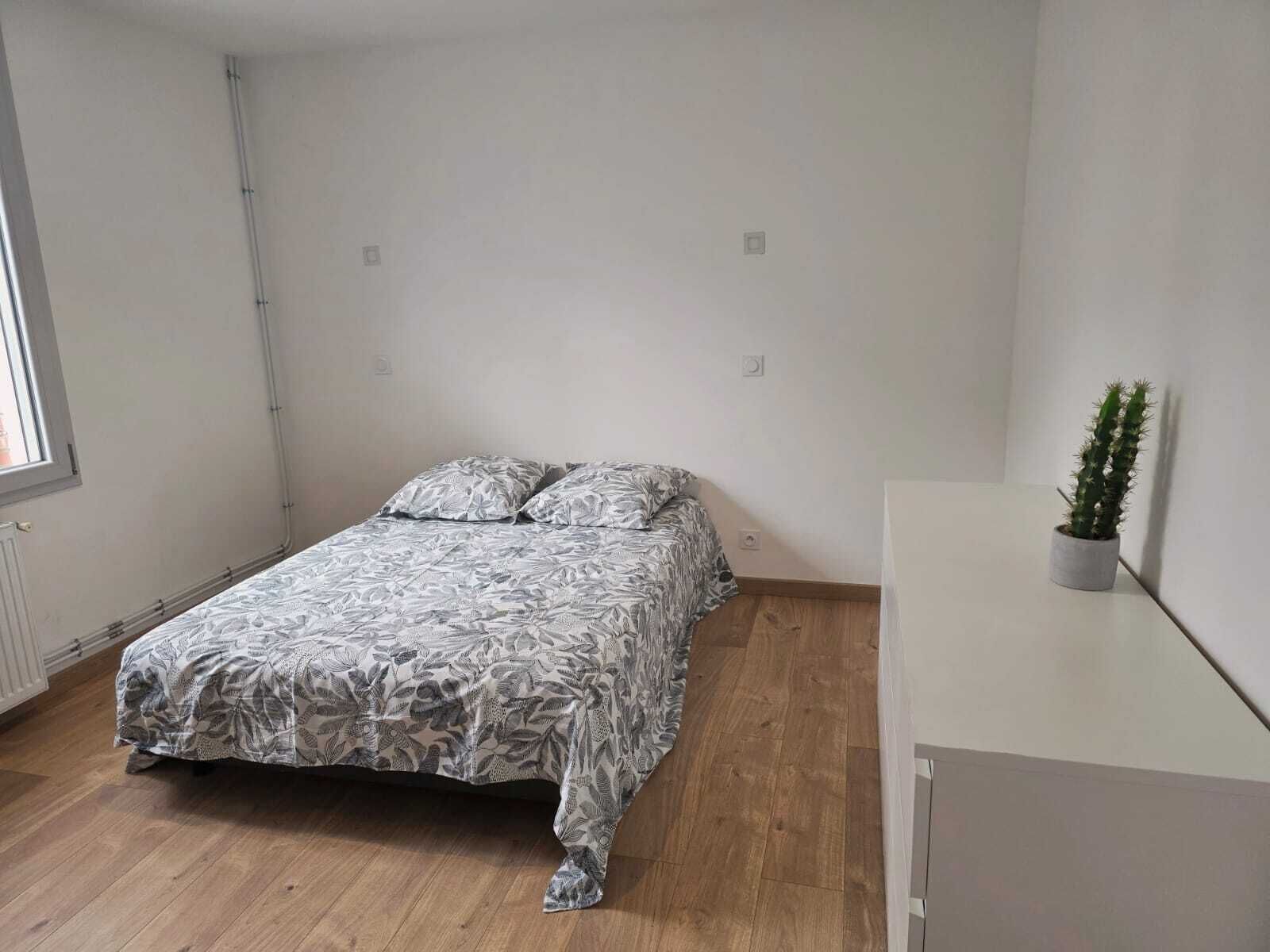 A bedroom with a bed, a potted plant, and a white cabinet.