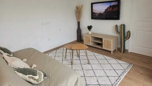 Ein Schlafzimmer mit einem Bett, einem Fernseher an der Wand, einem Kaktus und einem kleinen Tisch.