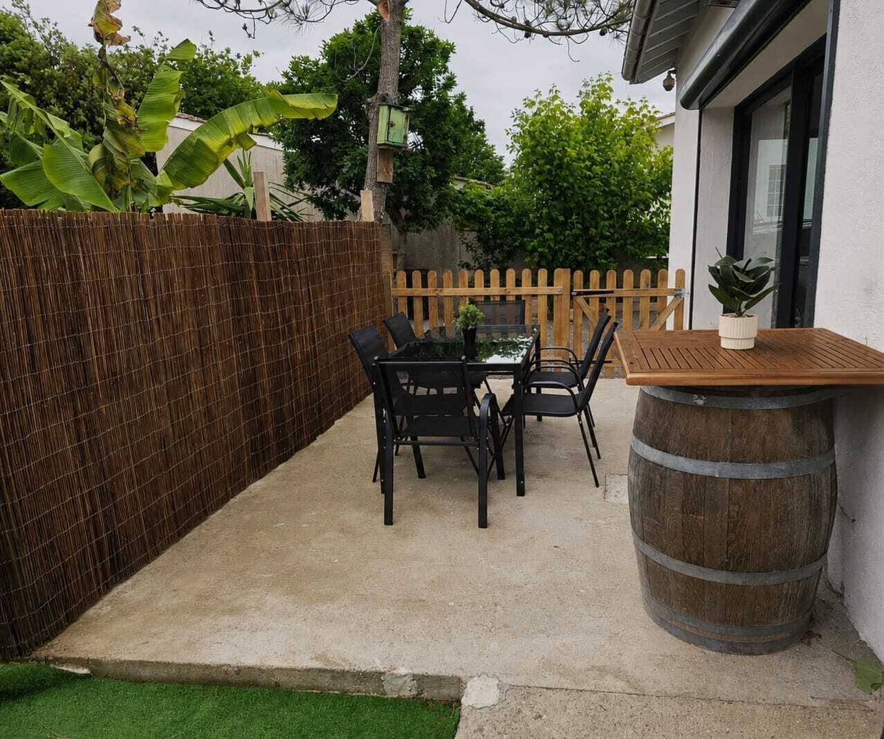A patio with a table and chairs, a wooden fence, and a barrel.