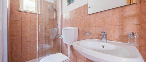 Un baño con ducha de vidrio, inodoro blanco y lavamanos blanco.