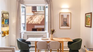 A dining area with a table, chairs, a vase with flowers, and a view through an open window. - Apartment San Trifone RiR Collection (Rome)