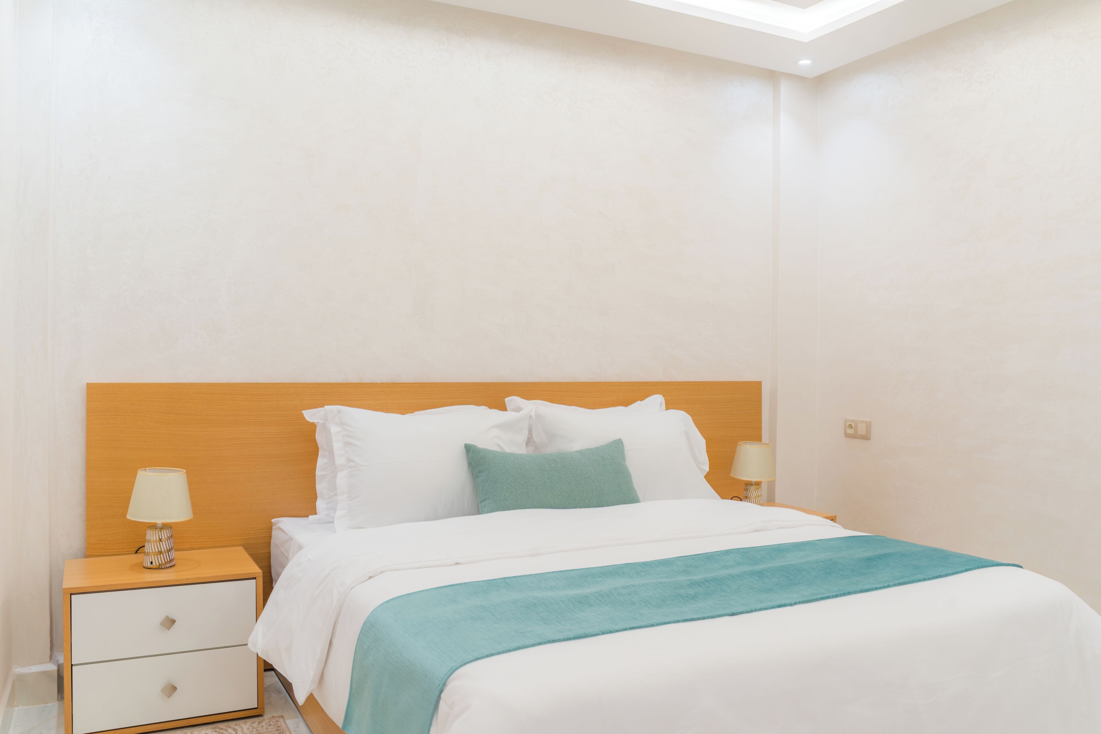 Quarto de hotel com cama, mesa de cabeceira, abajur e luz no teto.