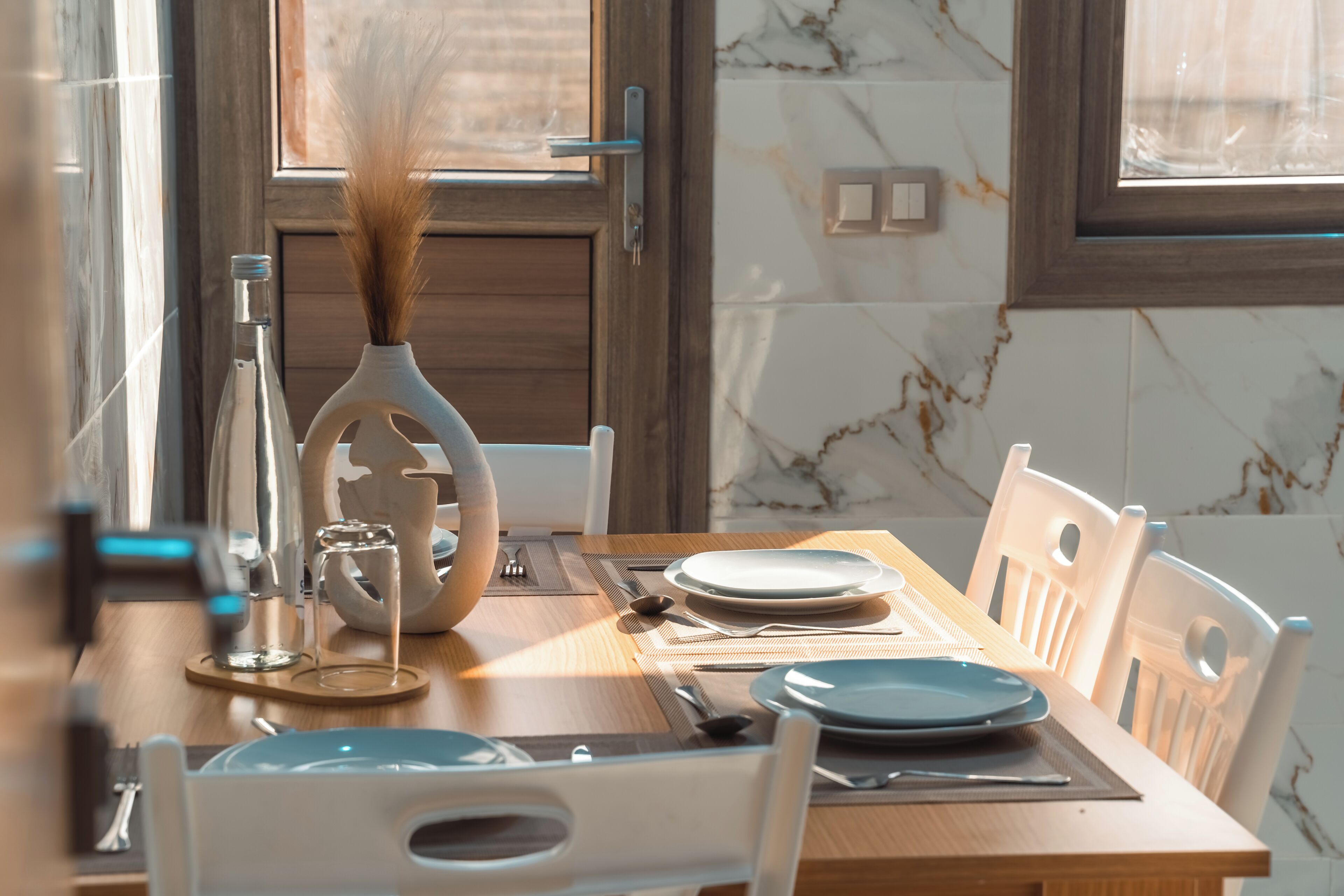 A dining table set with plates, cutlery, and a vase with dried plants.