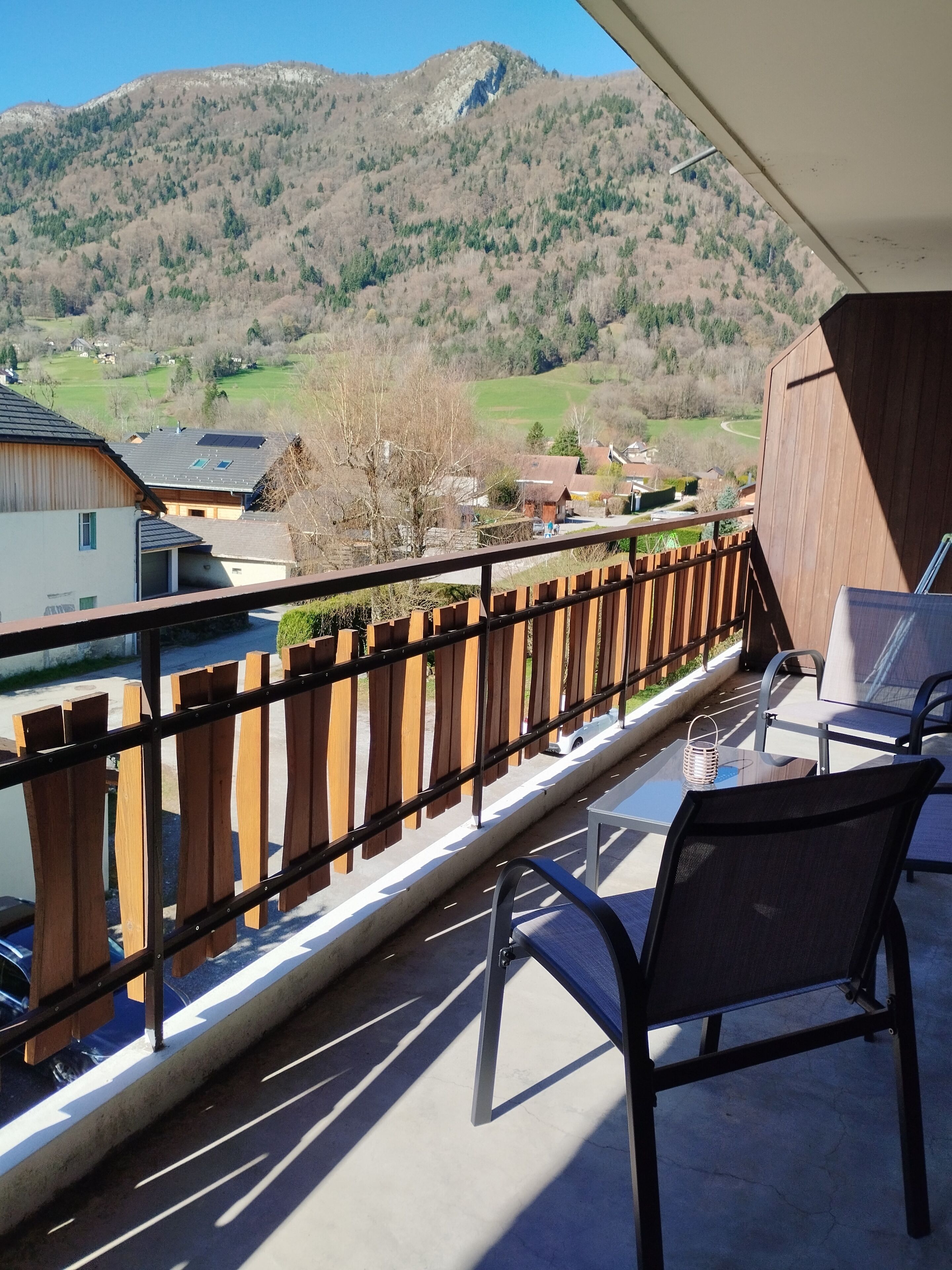 Un balcón con vistas a un paisaje montañoso, una valla de madera y una mesa con sillas.