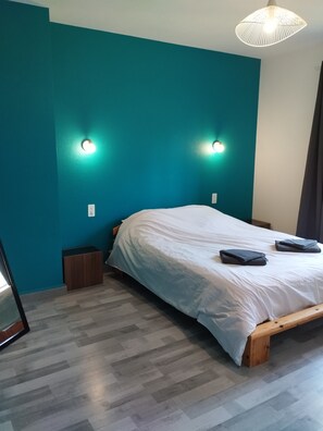 Ein Schlafzimmer mit türkisfarbenen Wänden, einem hölzernen Bettgestell, einer weißen Bettdecke, zwei Nachttischlampen und einem kleinen Nachttisch.