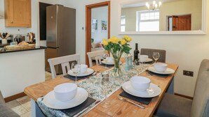 A dining area with a wooden table set for four, a kitchen with a refrigerator, and a mirror on the wall. - Lumford Mill Cottage (Bakewell)