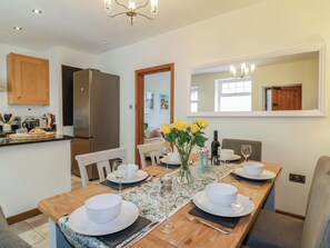A dining area with a wooden table set for four, a kitchen with a refrigerator, and a mirror on the wall. - Lumford Mill Cottage (Bakewell)