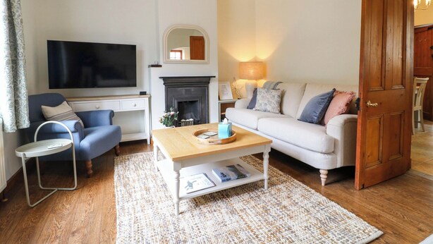 A living room with a sofa, a coffee table, a fireplace, a television, and a door. - Lumford Mill Cottage (Bakewell)