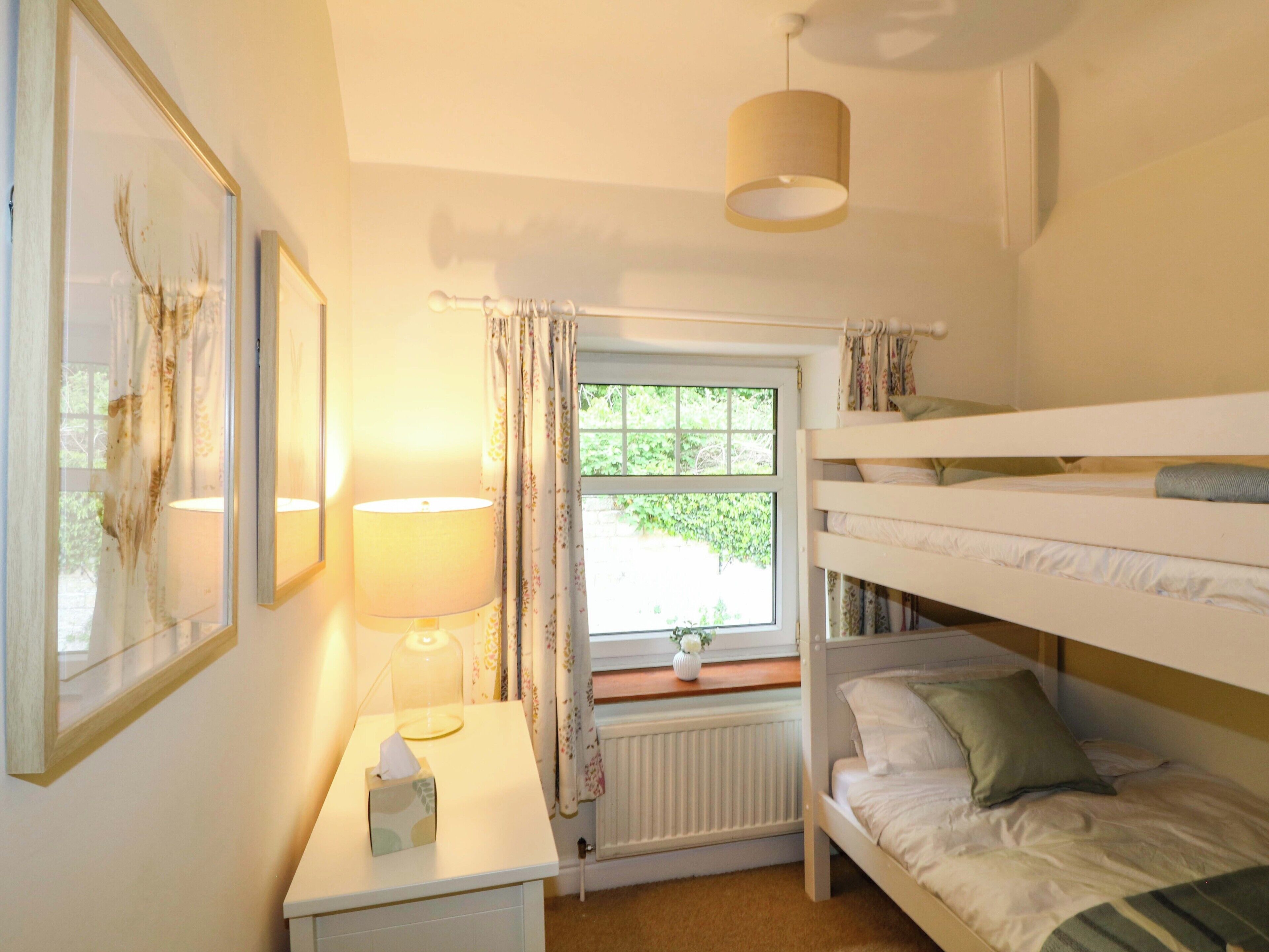 A bedroom with bunk beds, a bedside table with a lamp, a window with curtains, and a radiator.