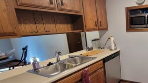 Una cocina con armarios de madera, un lavamanos de acero inoxidable, un microondas y un lavavajillas.
