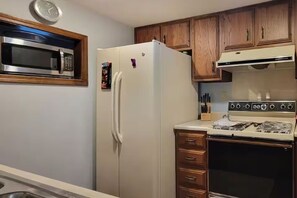Una cocina con microondas, refrigerador, estufa, gabinetes de madera y un reloj en la pared.