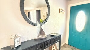 A dark wooden console table with a round mirror above it, a small clock, and a decorative sailboat model.