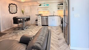 A modern kitchen with white cabinets, a stainless steel refrigerator, and a dining area with a black leather sofa.