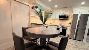 A modern kitchen with white cabinets, a stainless steel refrigerator, a microwave, and a dining area with a round table and chairs.