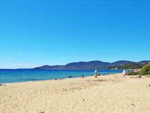 Ein Strand mit klarem, blauem Wasser, sandigem Ufer und Bergen in der Ferne.