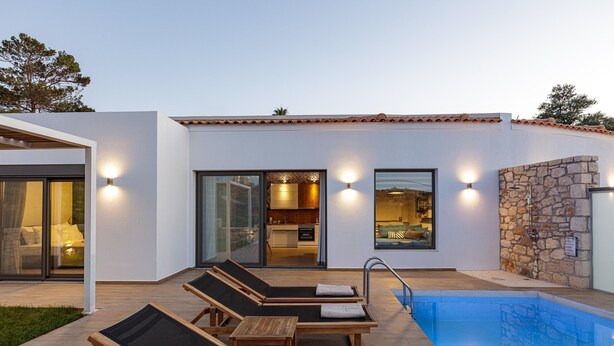 Ett modernt hus med en swimmingpool, solstolar och ett kök som är öppet och synligt.