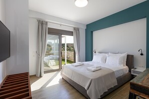 Ein Schlafzimmer mit Bett, Fernseher, einer Holzbank, einem Nachttisch und Blick durch eine Glastür.