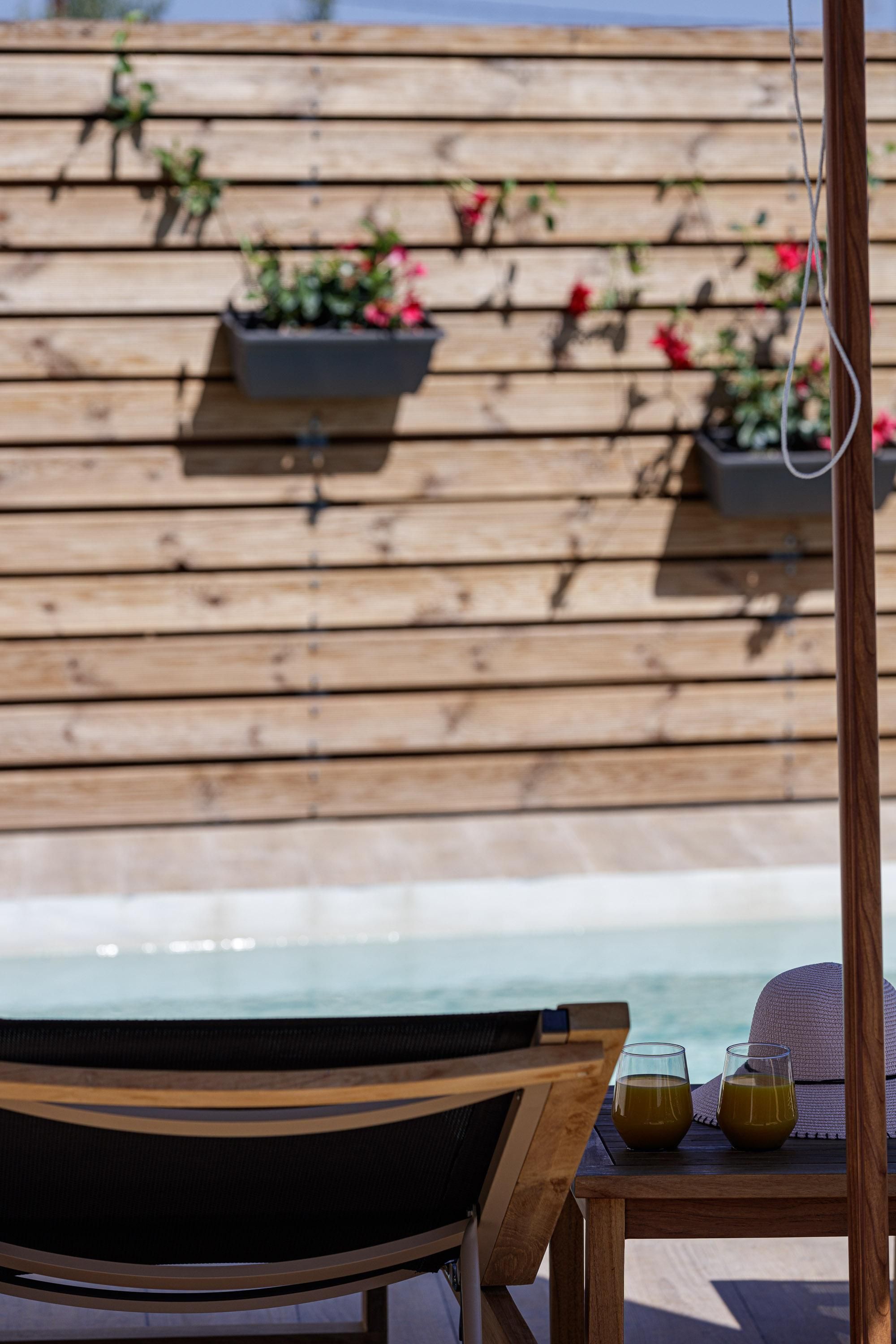 A wooden deck with a chair, two glasses of drink, and a straw hat.