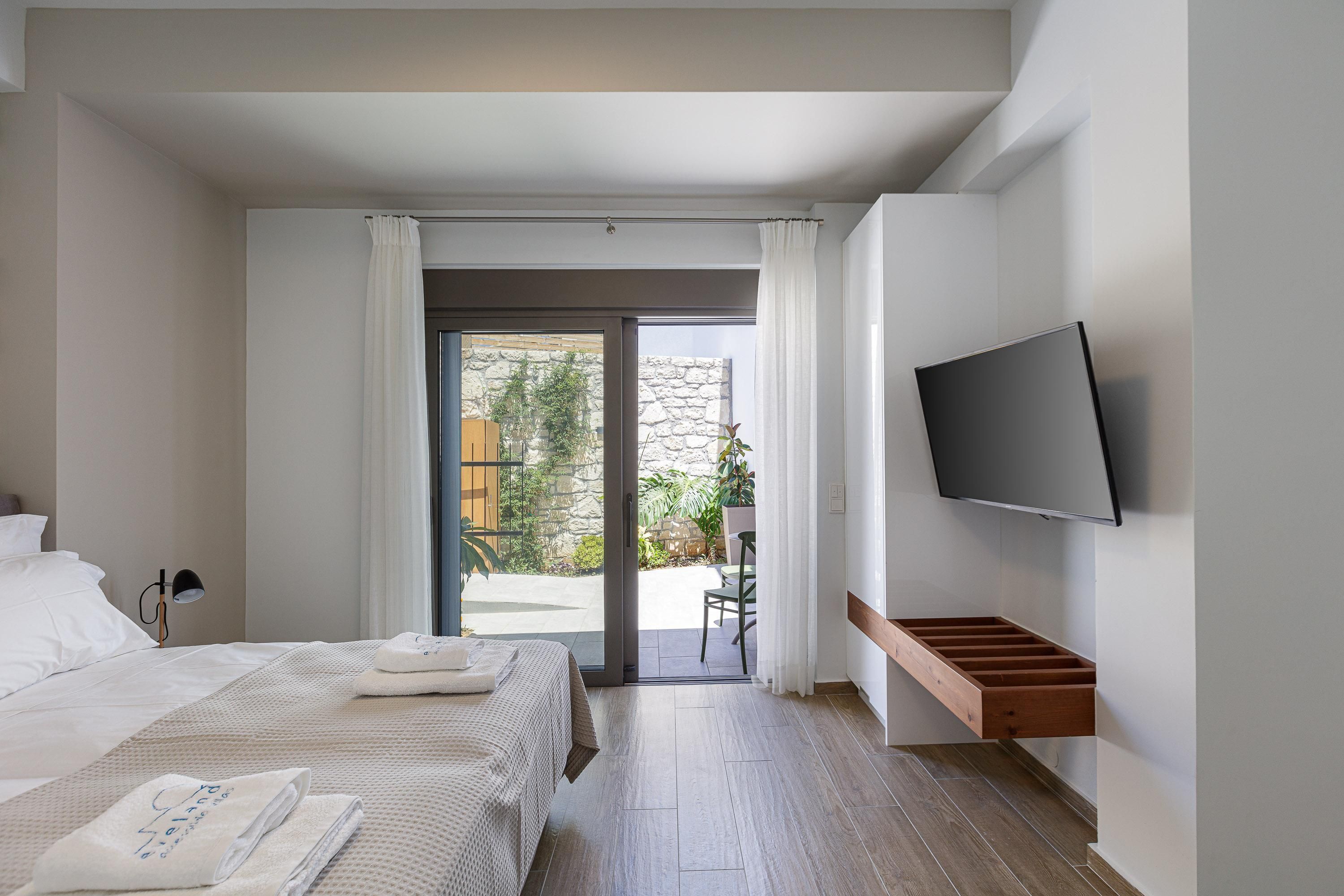 Ein modernes Hotelzimmer mit Bett, Flachbildfernseher, einer Schiebeglastür zu einem Balkon und einer Holzbank.