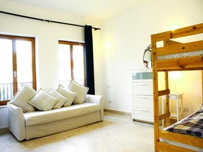 A room with a bunk bed, a sofa with cushions, a desk, and a window with curtains.