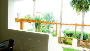 Un balcon donnant sur une pelouse verdoyante et des palmiers, une petite table avec des chaises et une balustrade en bois.