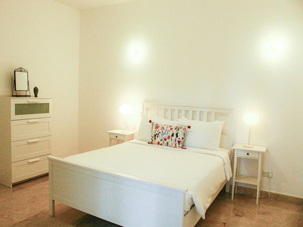 A neatly arranged bedroom with a bed, bedside tables, a dresser, and a mirror.
