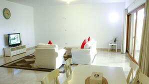 Un salon moderne avec des meubles blancs, un téléviseur et un coin repas comprenant une table et des chaises.